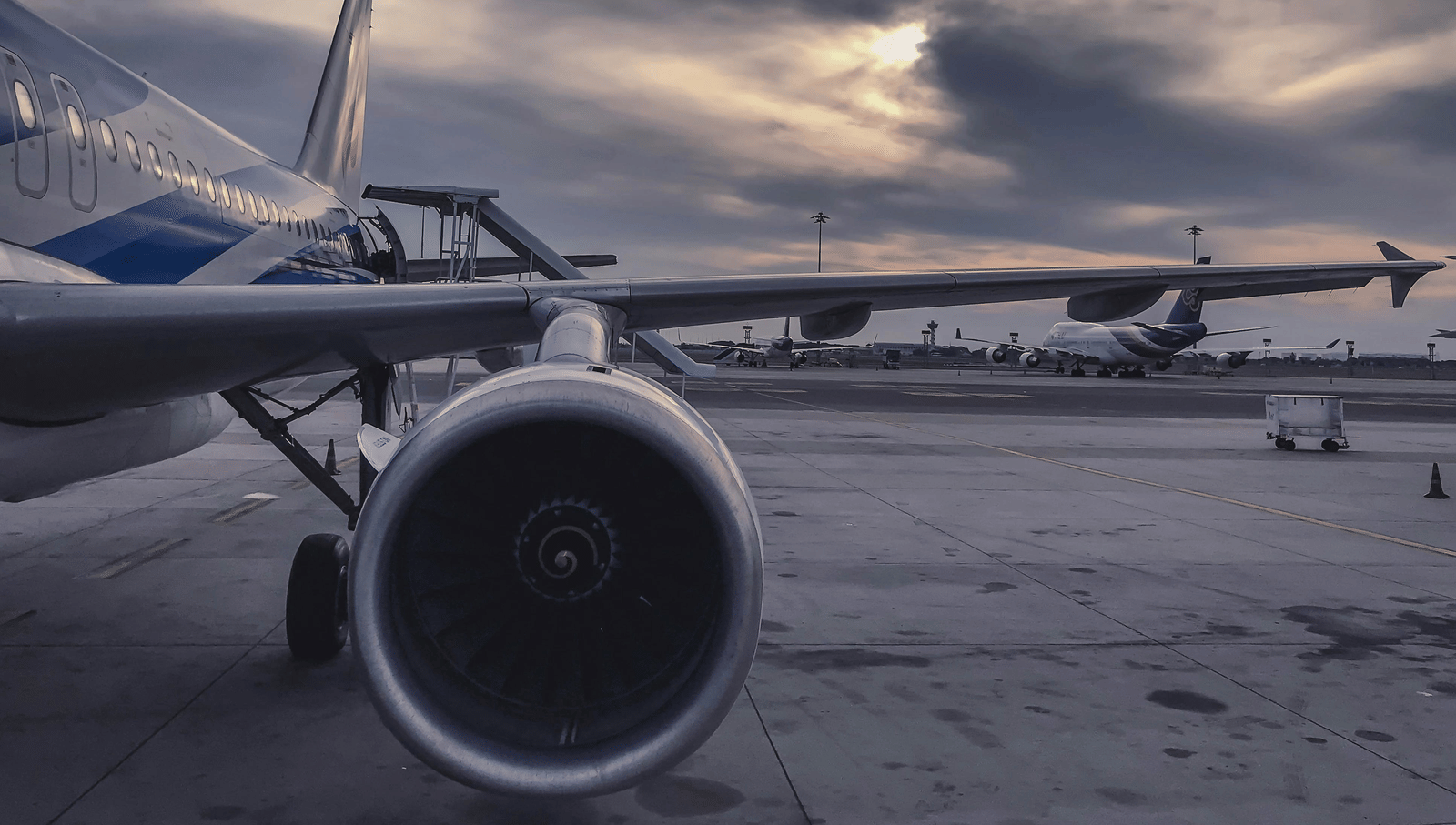 An aircraft parked in an airport with a cloudy sky in the background.